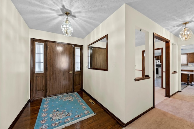 foyer with a textured ceiling, an inviting chandelier, and carpet flooring