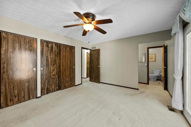 unfurnished bedroom with ensuite bathroom, two closets, ceiling fan, light colored carpet, and a textured ceiling