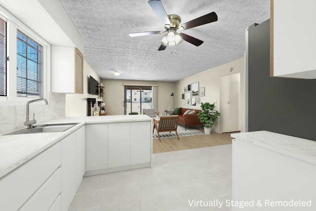 kitchen featuring ceiling fan, kitchen peninsula, sink, a textured ceiling, and white cabinets