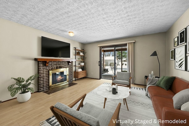 living room with a brick fireplace, a textured ceiling, and light hardwood / wood-style flooring