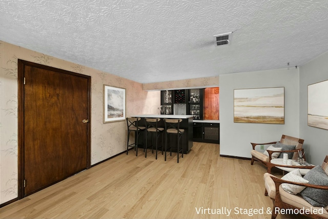 kitchen featuring a textured ceiling, a breakfast bar area, light hardwood / wood-style flooring, and kitchen peninsula