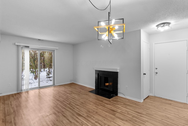 unfurnished living room with a fireplace, a textured ceiling, light hardwood / wood-style flooring, and an inviting chandelier