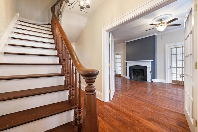 staircase featuring hardwood / wood-style flooring, ceiling fan with notable chandelier, and ornamental molding