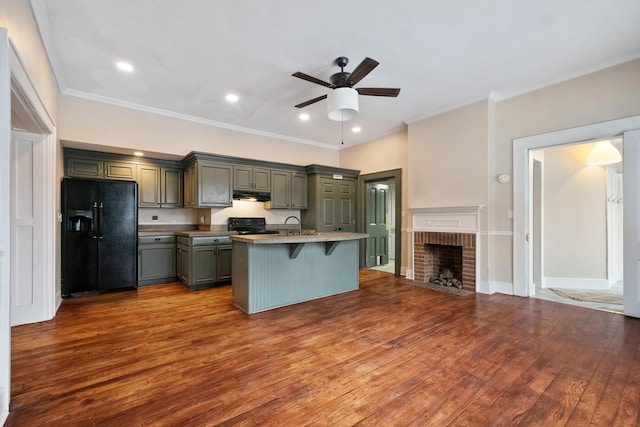 kitchen featuring black appliances, light hardwood / wood-style flooring, a brick fireplace, an island with sink, and a kitchen bar