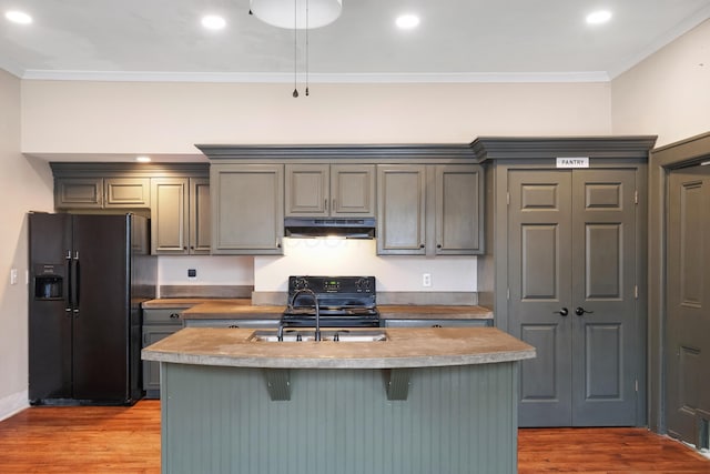 kitchen featuring a kitchen island with sink, sink, black appliances, and light wood-type flooring