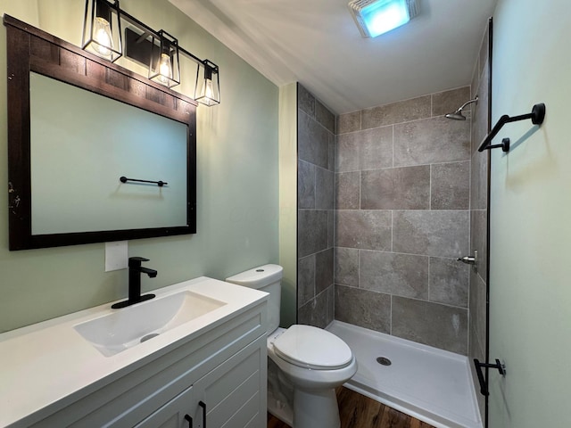 bathroom featuring a tile shower, hardwood / wood-style floors, vanity, and toilet