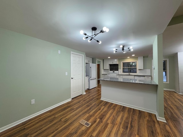 kitchen with an inviting chandelier, white cabinets, white fridge, light stone counters, and kitchen peninsula