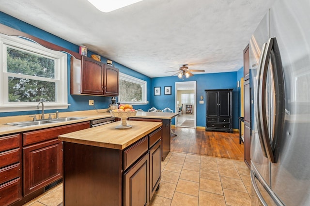 kitchen featuring stainless steel refrigerator with ice dispenser, ceiling fan, sink, light tile patterned floors, and a kitchen island