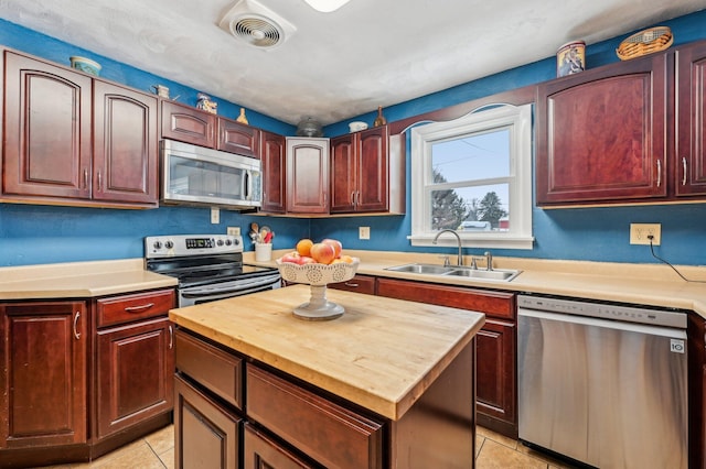 kitchen with wood counters, appliances with stainless steel finishes, sink, a center island, and light tile patterned flooring