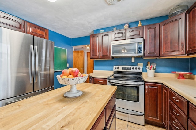 kitchen with light tile patterned floors, a textured ceiling, appliances with stainless steel finishes, and wooden counters