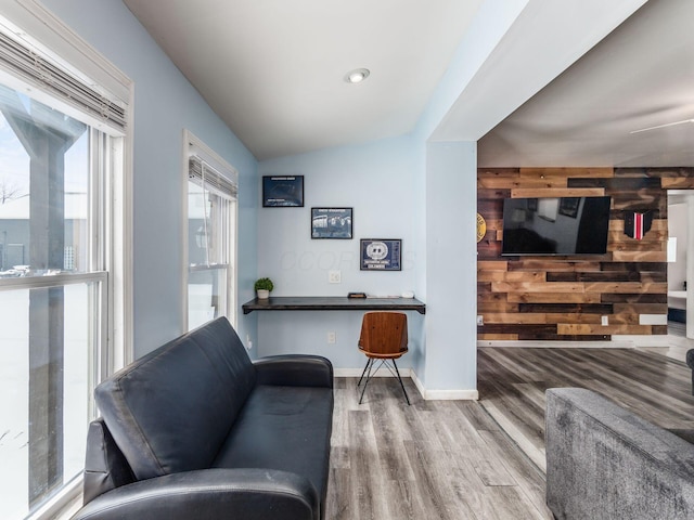 living room with wooden walls, built in desk, vaulted ceiling, and hardwood / wood-style flooring