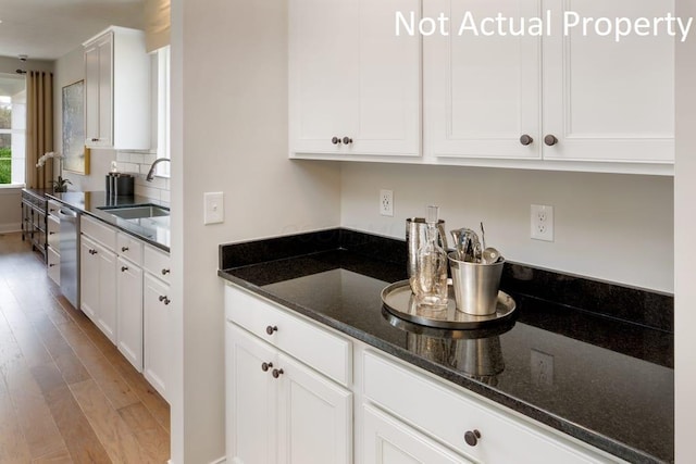 kitchen with dishwasher, sink, dark stone countertops, white cabinets, and light wood-type flooring