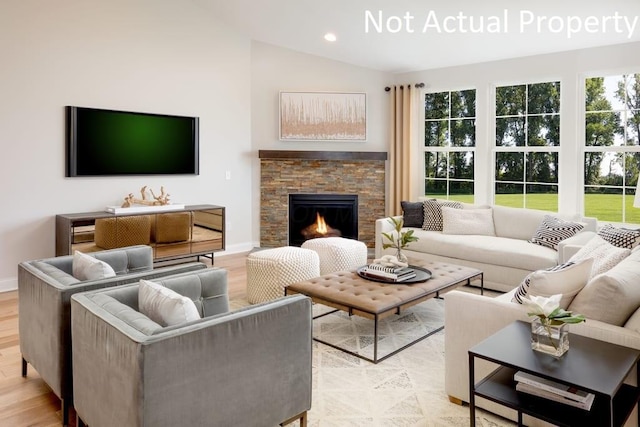 living room with vaulted ceiling, a stone fireplace, a healthy amount of sunlight, and light hardwood / wood-style floors