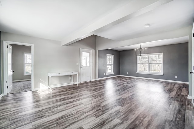 unfurnished living room featuring dark wood-type flooring, a healthy amount of sunlight, and an inviting chandelier