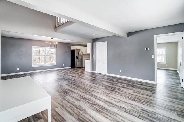 unfurnished living room featuring hardwood / wood-style flooring, a wealth of natural light, beam ceiling, and an inviting chandelier