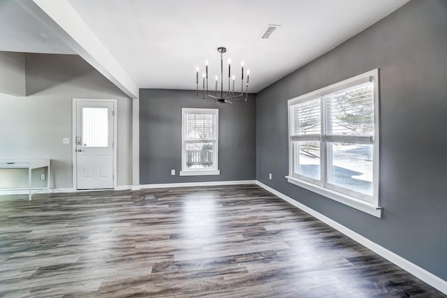 unfurnished dining area with dark wood-type flooring, a wealth of natural light, and a notable chandelier