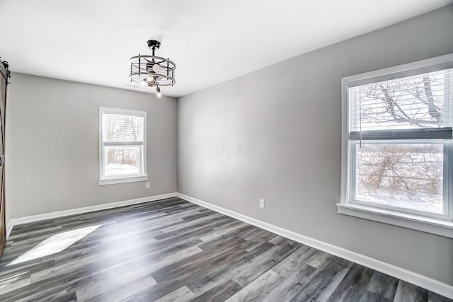 spare room featuring dark wood-type flooring, a notable chandelier, and a barn door