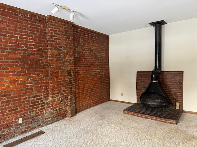 unfurnished living room with rail lighting, a wood stove, light carpet, and brick wall