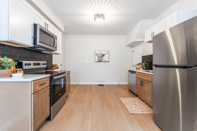 kitchen with decorative backsplash, appliances with stainless steel finishes, light hardwood / wood-style floors, and white cabinetry