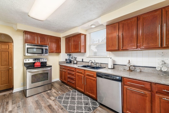 kitchen featuring backsplash, a textured ceiling, stainless steel appliances, dark wood-type flooring, and sink