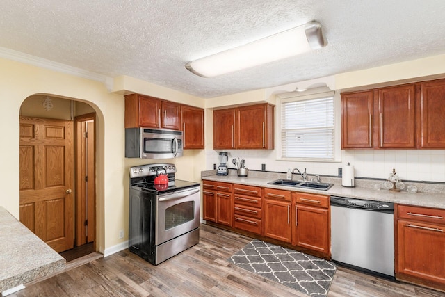 kitchen with sink, dark hardwood / wood-style floors, a textured ceiling, appliances with stainless steel finishes, and ornamental molding