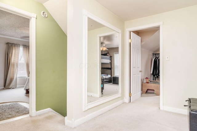 corridor featuring a textured ceiling, light carpet, and vaulted ceiling