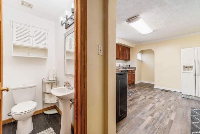 kitchen with light wood-type flooring, a textured ceiling, and white fridge with ice dispenser