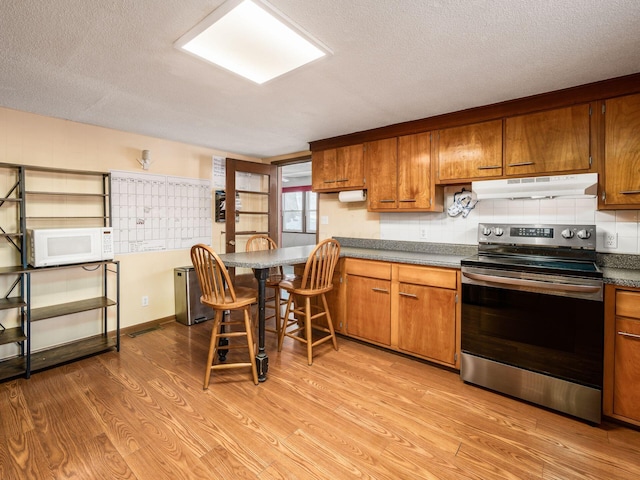 kitchen featuring stainless steel electric stove, light hardwood / wood-style floors, a textured ceiling, and decorative backsplash