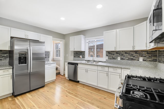 kitchen with decorative backsplash, appliances with stainless steel finishes, light wood-type flooring, sink, and white cabinetry