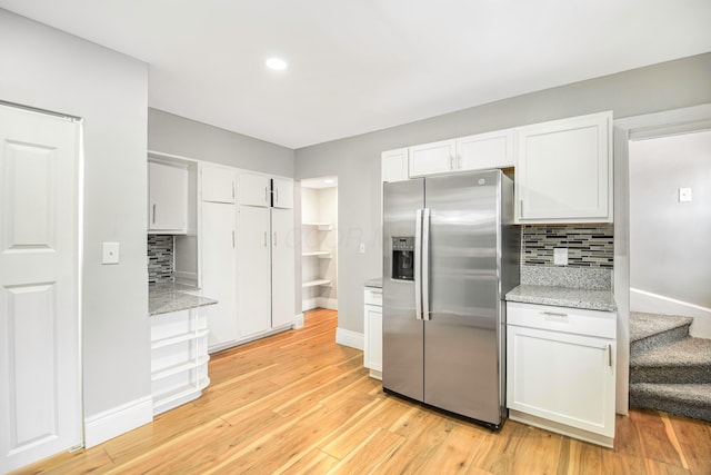 kitchen with white cabinetry, light stone countertops, stainless steel fridge with ice dispenser, backsplash, and light hardwood / wood-style floors