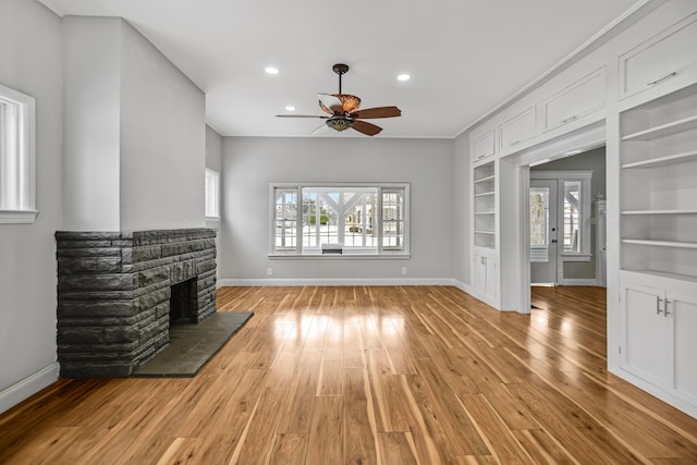 unfurnished living room featuring a fireplace, light hardwood / wood-style flooring, built in features, and ceiling fan