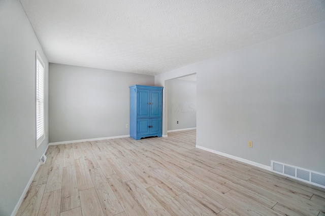 empty room with a textured ceiling and light hardwood / wood-style flooring