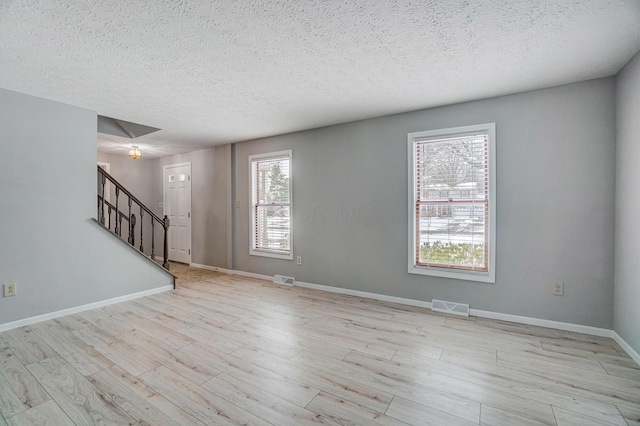 spare room with plenty of natural light, a textured ceiling, and light hardwood / wood-style flooring