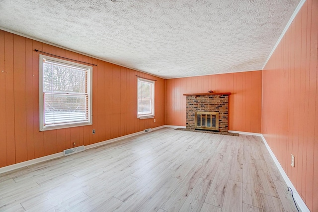 unfurnished living room with a brick fireplace, a wealth of natural light, and wooden walls