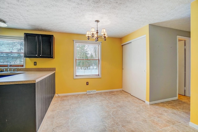 kitchen with sink, pendant lighting, a textured ceiling, and a notable chandelier