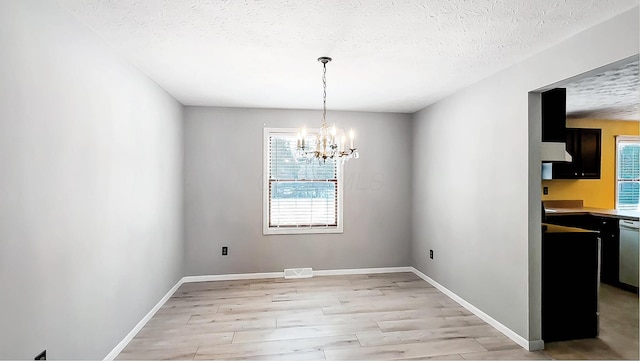 unfurnished dining area with light hardwood / wood-style floors, a chandelier, and a textured ceiling