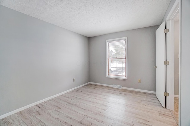 spare room with light wood-type flooring and a textured ceiling