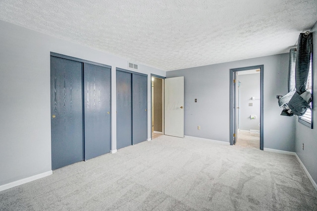 bedroom with light colored carpet, a textured ceiling, and multiple closets