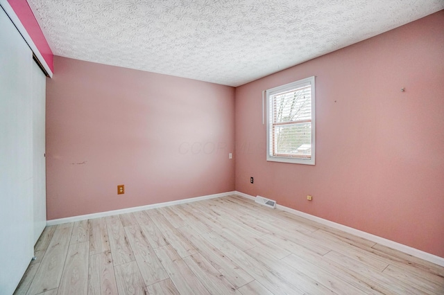 unfurnished room featuring light wood-type flooring and a textured ceiling