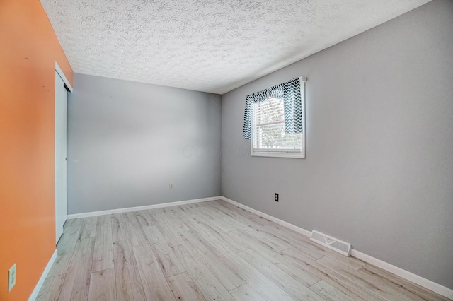 unfurnished room with a textured ceiling and light hardwood / wood-style floors