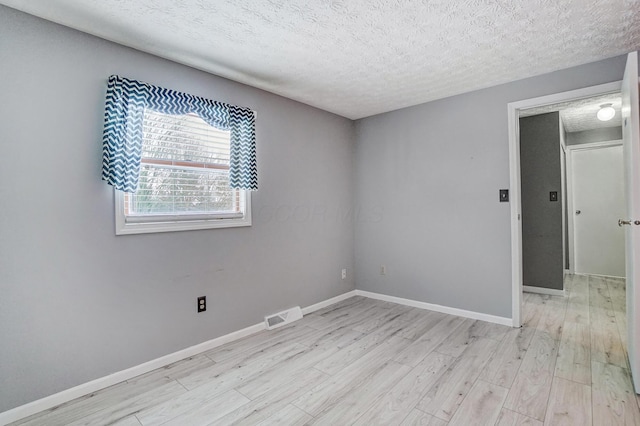 empty room with a textured ceiling and light hardwood / wood-style flooring