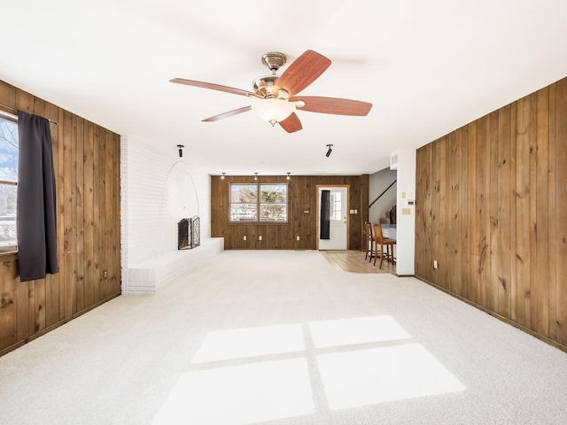 unfurnished living room featuring ceiling fan, a brick fireplace, light carpet, and wood walls