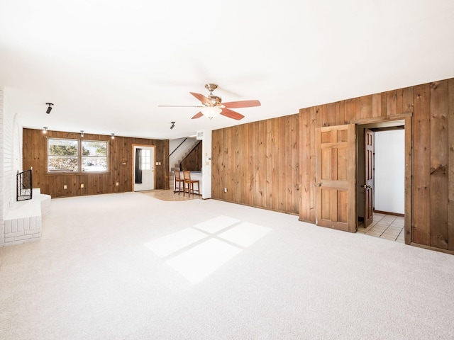 unfurnished living room featuring ceiling fan, wooden walls, and light carpet