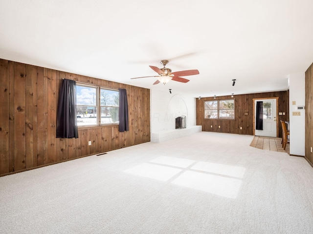 unfurnished living room featuring a fireplace, light colored carpet, wood walls, and ceiling fan