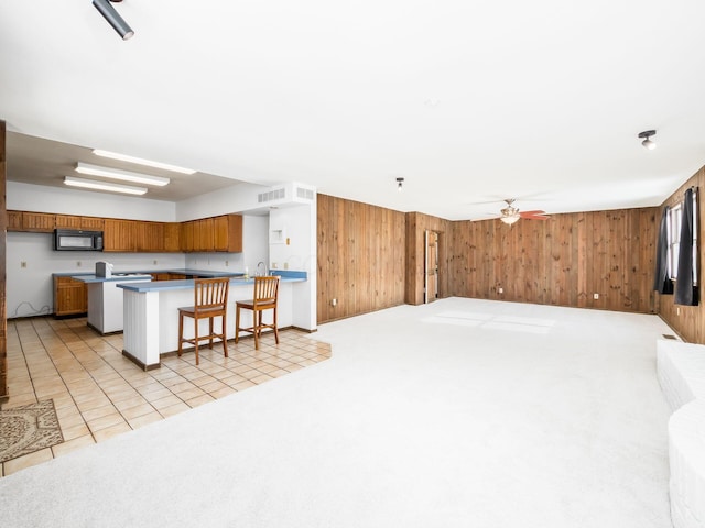 kitchen featuring a breakfast bar area, wood walls, ceiling fan, and light colored carpet