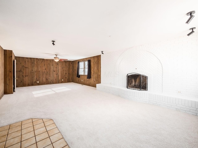 unfurnished living room with ceiling fan, a brick fireplace, wooden walls, and light carpet