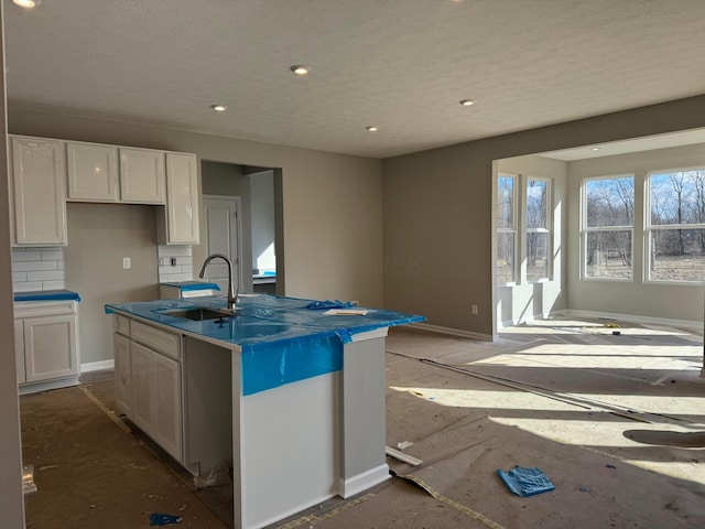 kitchen with baseboards, white cabinets, a sink, and a center island with sink