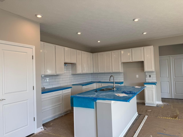 kitchen with white cabinets, a sink, backsplash, and an island with sink