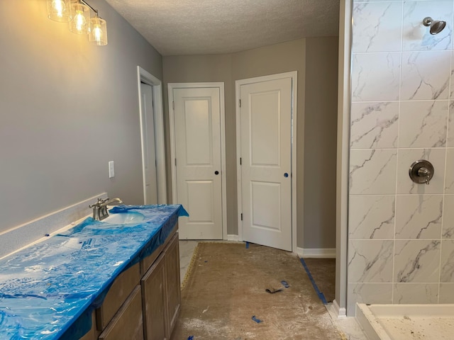 full bath with a textured ceiling, tiled shower, and vanity