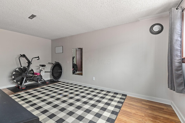 workout area with hardwood / wood-style floors, a textured ceiling, and wooden walls